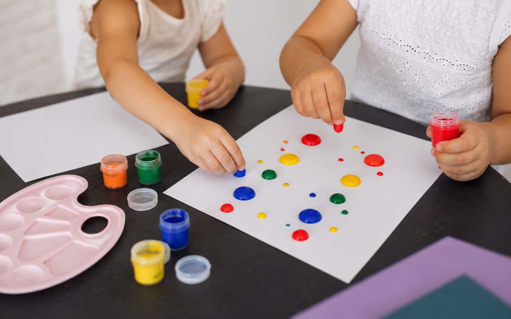 Des enfants déposent des gouttes de peinture colorée sur une feuille blanche avant de la plier pour créer un papillon symétrique.